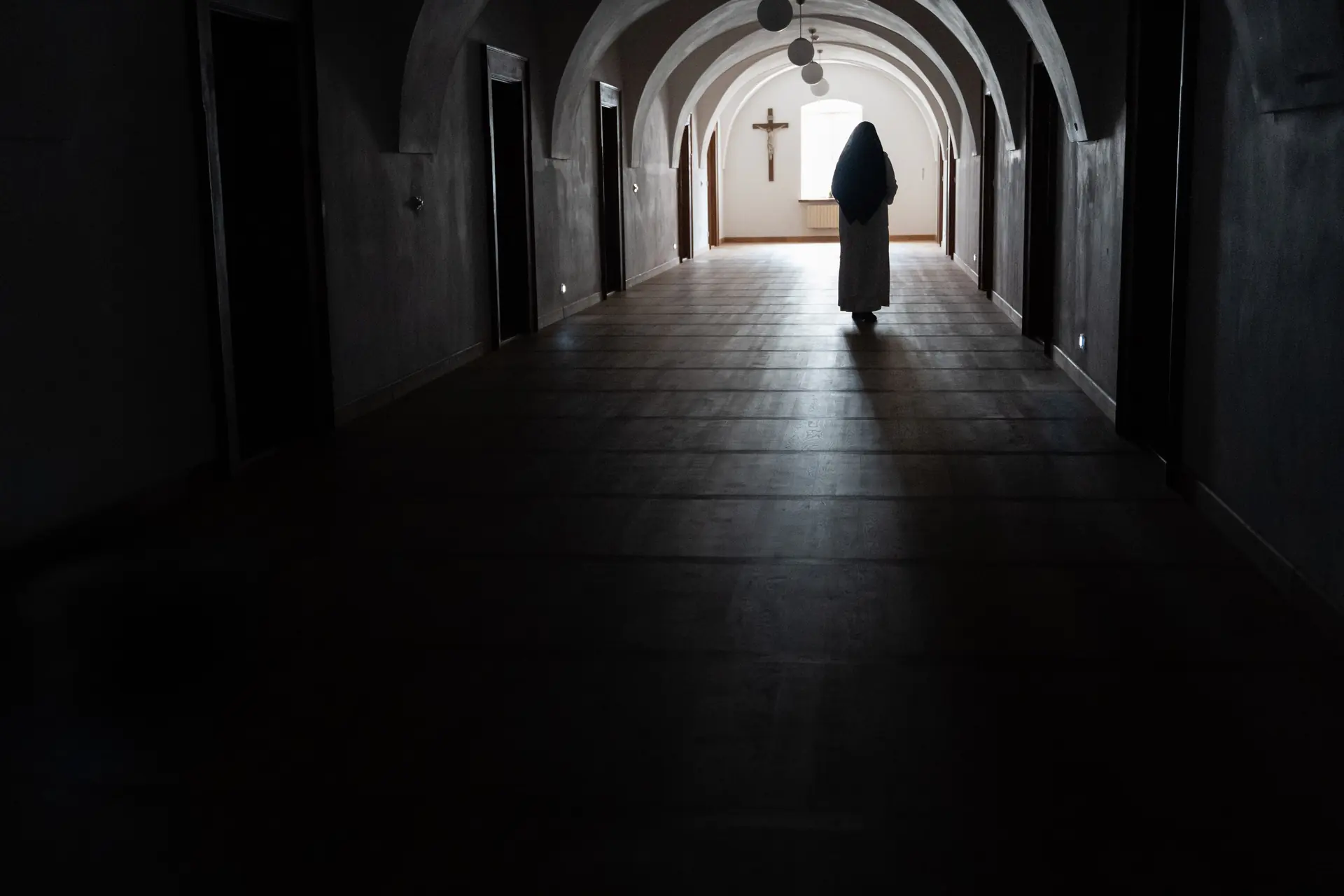 Řeholnice kráčí klenutou klášterní chodbou ke světlu