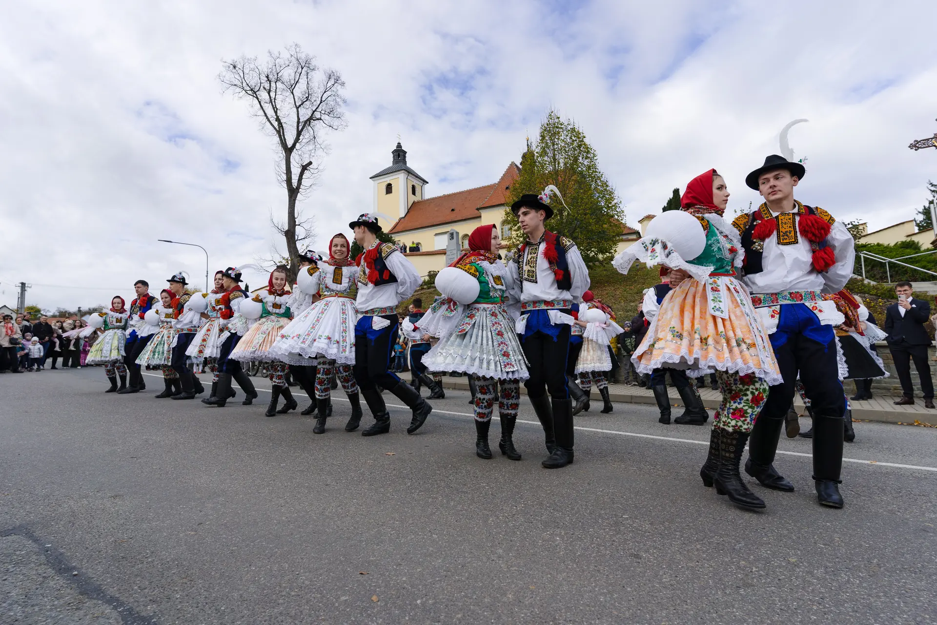 Krojovaný průvod tančí na silnici před kostelem