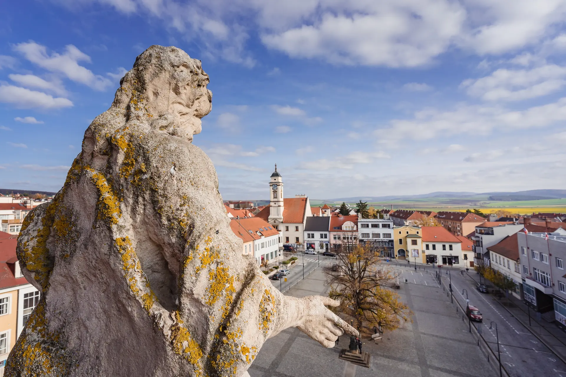 Kamenná socha shlíží na náměstí a střechy Uherského Brodu
